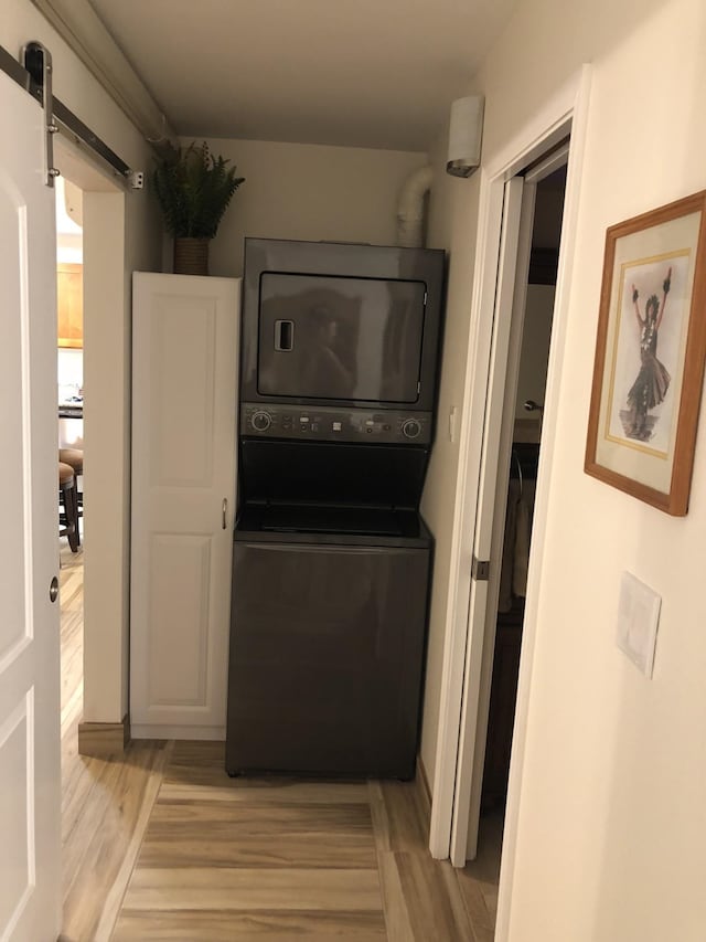 kitchen with stacked washer and clothes dryer, a barn door, and light hardwood / wood-style flooring