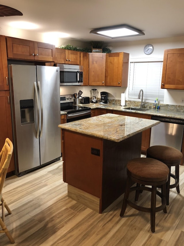 kitchen featuring sink, appliances with stainless steel finishes, light stone counters, a kitchen island, and light wood-type flooring