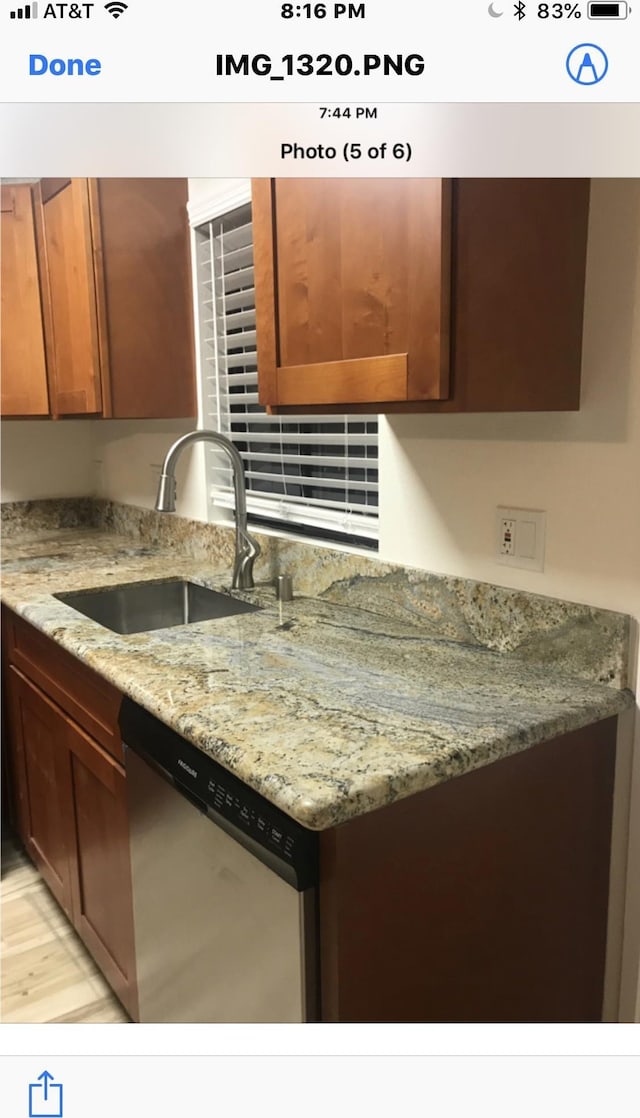 kitchen featuring light stone counters, stainless steel dishwasher, and sink