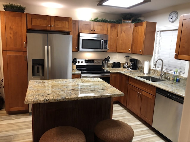 kitchen with stainless steel appliances, light stone countertops, a center island, and sink