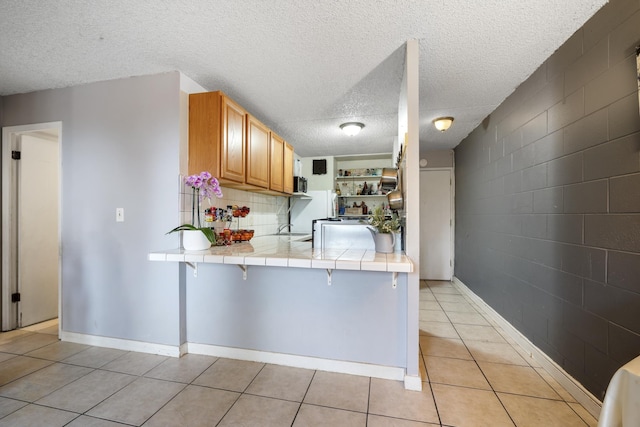 kitchen with tile countertops, light tile patterned floors, a peninsula, open shelves, and stainless steel microwave