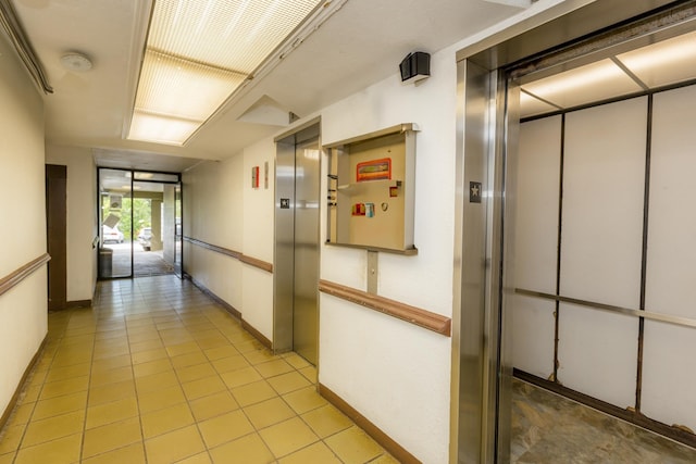 hall with elevator, light tile patterned floors, and baseboards