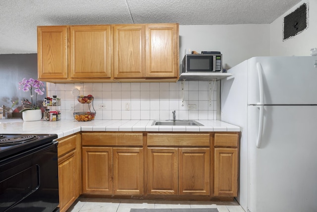 kitchen featuring stainless steel microwave, black range with electric cooktop, decorative backsplash, freestanding refrigerator, and a sink