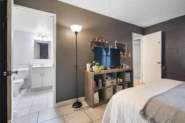 bedroom with tile walls, light tile patterned floors, ensuite bathroom, a textured ceiling, and a sink