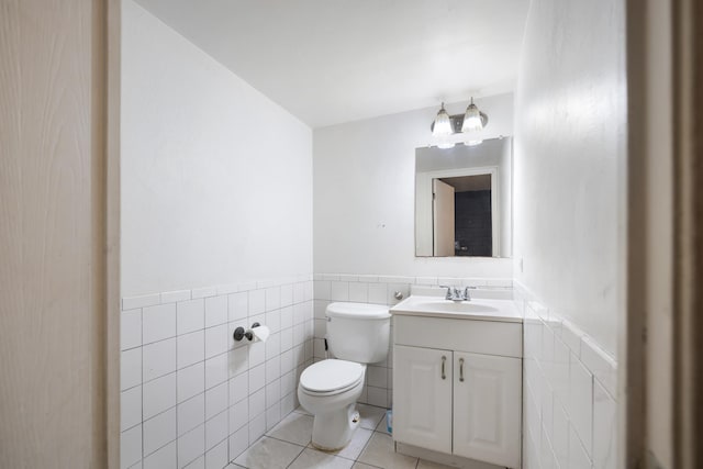 half bath with tile patterned flooring, tile walls, toilet, and a wainscoted wall