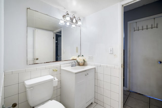 bathroom with tile patterned floors, toilet, tile walls, wainscoting, and vanity