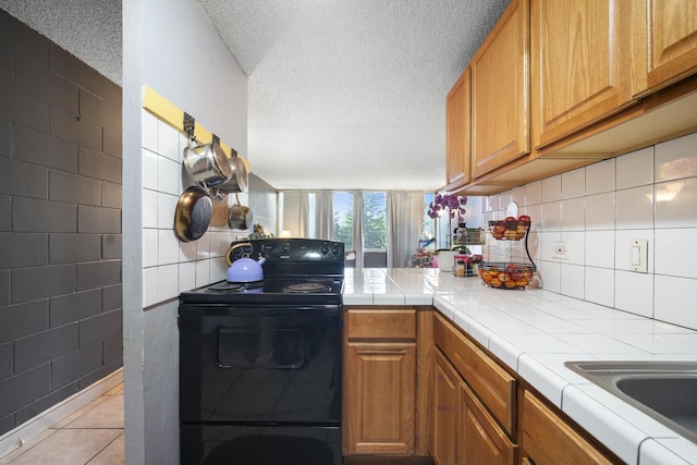 kitchen with tile counters, electric range, brown cabinets, and a textured ceiling