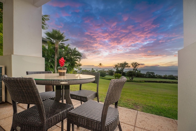 patio terrace at dusk featuring a lawn and a water view