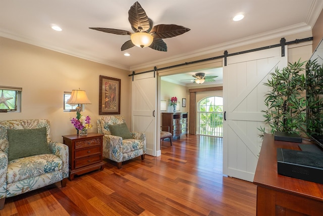 sitting room featuring a barn door, hardwood / wood-style flooring, ceiling fan, and ornamental molding