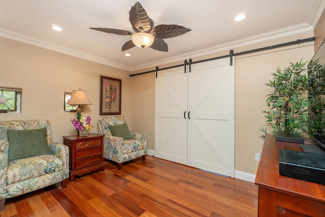 sitting room featuring a barn door, hardwood / wood-style flooring, ceiling fan, and crown molding