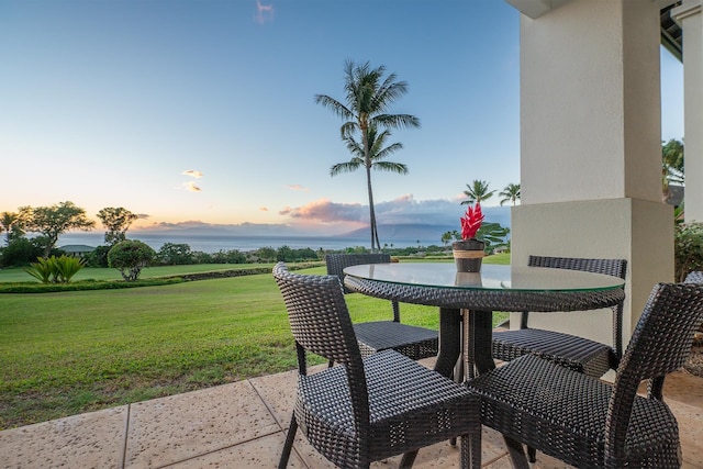 patio terrace at dusk featuring a yard and a water view