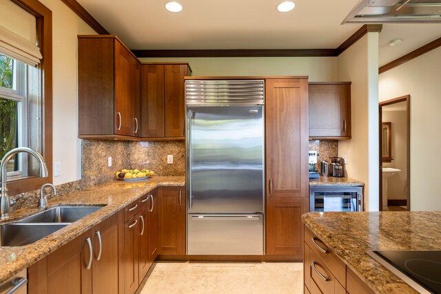 kitchen with light stone counters, sink, stainless steel built in refrigerator, and ornamental molding