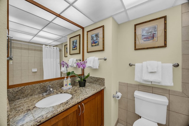 bathroom featuring vanity, toilet, tile walls, a shower with shower curtain, and a drop ceiling