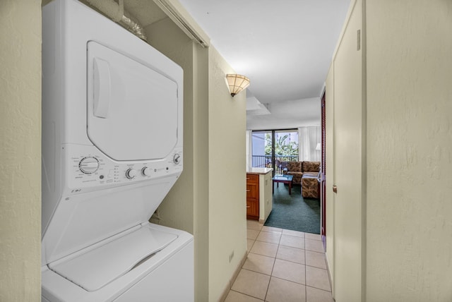 washroom featuring laundry area, stacked washing maching and dryer, a textured wall, and light tile patterned floors