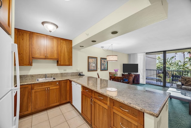 kitchen with light stone countertops, brown cabinets, a sink, a peninsula, and white appliances