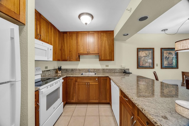 kitchen with brown cabinetry, a sink, white appliances, and light stone countertops