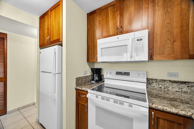 kitchen featuring brown cabinets, light stone countertops, white appliances, and light tile patterned flooring