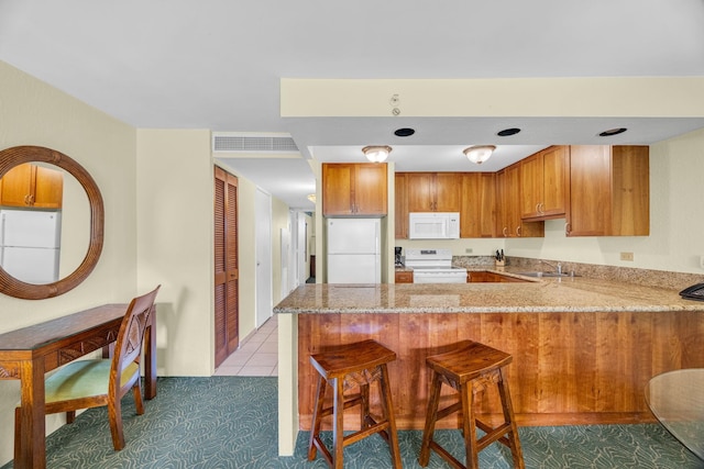 kitchen with light stone countertops, brown cabinets, a sink, a peninsula, and white appliances