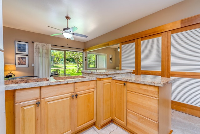 kitchen with ceiling fan, light stone counters, kitchen peninsula, and light brown cabinetry