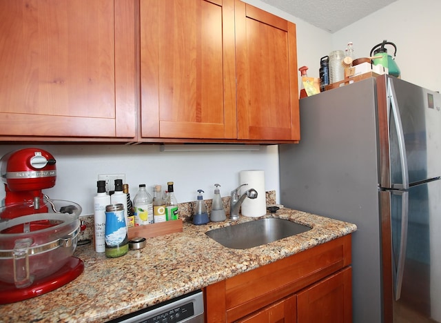 kitchen featuring a textured ceiling, stainless steel fridge, light stone countertops, and sink