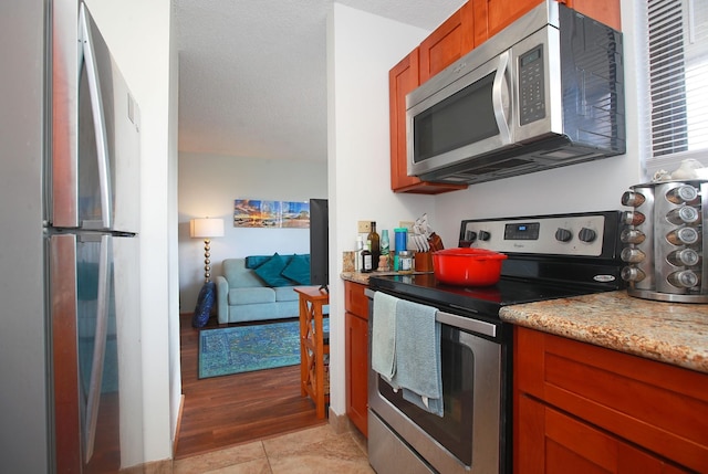 kitchen featuring light stone countertops, light hardwood / wood-style flooring, stainless steel appliances, and a textured ceiling