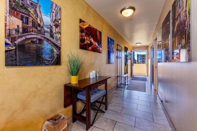hallway featuring a textured wall, tile patterned floors, and baseboards
