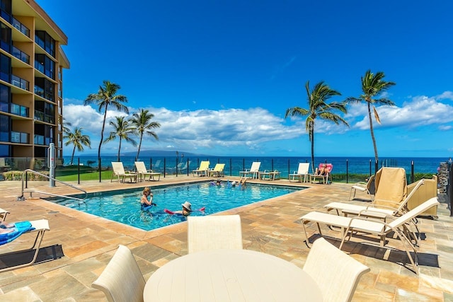 community pool featuring fence, a water view, and a patio area