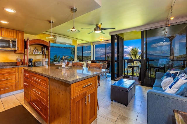 kitchen with dark stone counters, stainless steel microwave, light tile patterned floors, ceiling fan, and pendant lighting