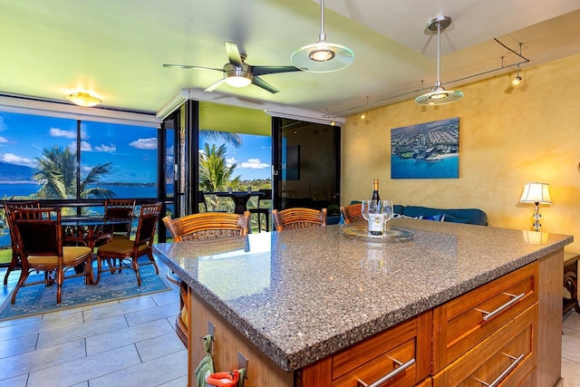 kitchen with pendant lighting, a kitchen island, light tile patterned flooring, a ceiling fan, and brown cabinetry