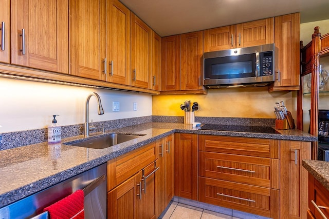 kitchen with dark stone countertops, stainless steel appliances, brown cabinetry, and a sink