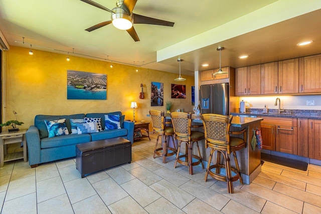 kitchen featuring a kitchen breakfast bar, light tile patterned floors, a sink, ceiling fan, and stainless steel refrigerator with ice dispenser