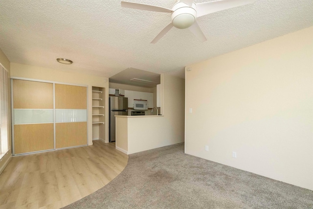 unfurnished living room with ceiling fan, light hardwood / wood-style floors, and a textured ceiling