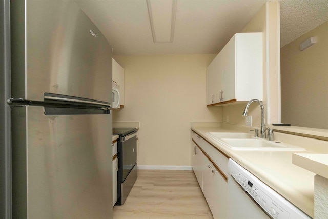 kitchen with stainless steel appliances, sink, white cabinetry, light hardwood / wood-style flooring, and a textured ceiling