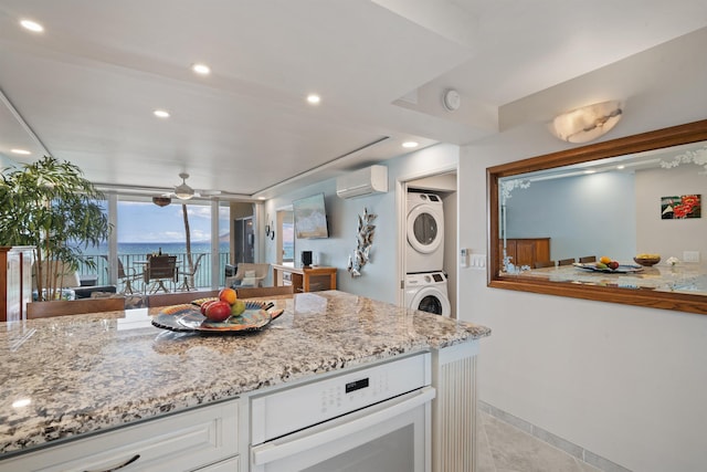 2430 S Kihei Rd Unit 411, Kihei, HI 96753 - kitchen featuring stacked washer and clothes dryer, a wall mounted air conditioner, white oven, ceiling fan, and light stone countertops