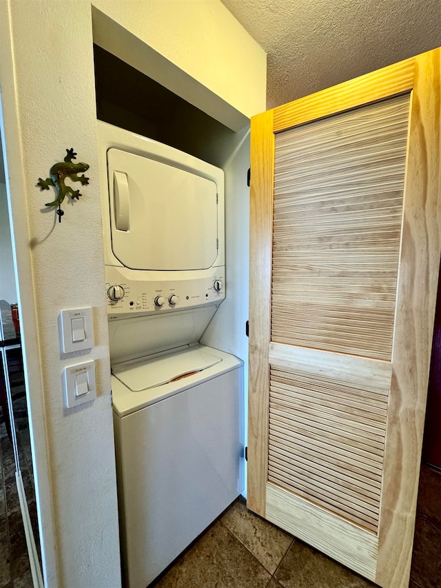 laundry room with dark tile floors and stacked washer and dryer