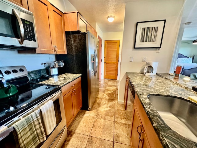 kitchen featuring stainless steel appliances, light tile flooring, ceiling fan, dark stone countertops, and sink