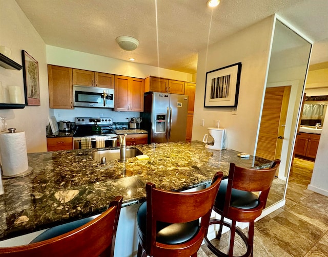 kitchen with a breakfast bar, light tile floors, stainless steel appliances, dark stone countertops, and sink