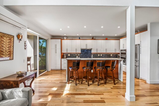 kitchen with a center island with sink, light hardwood / wood-style flooring, white cabinetry, a breakfast bar area, and stainless steel appliances