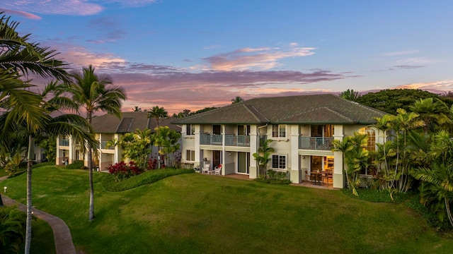 back house at dusk with a lawn and a balcony