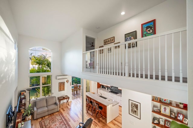 interior space with ceiling fan, sink, an AC wall unit, a towering ceiling, and light wood-type flooring