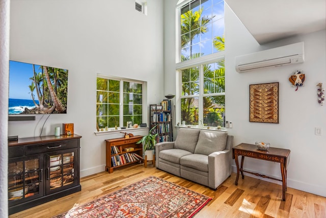 living area with a high ceiling, light hardwood / wood-style floors, an AC wall unit, and a wealth of natural light