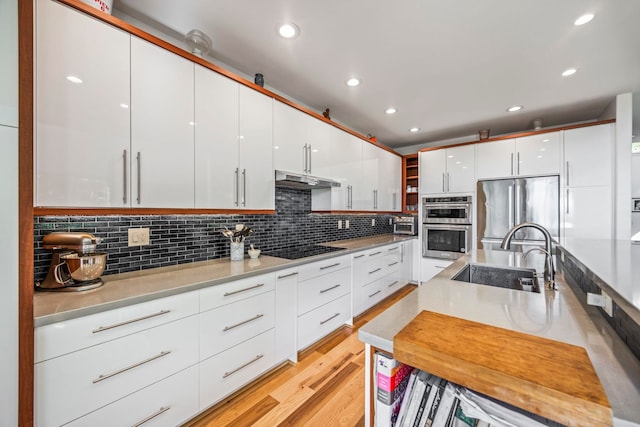 kitchen with white cabinetry, sink, light hardwood / wood-style flooring, backsplash, and appliances with stainless steel finishes