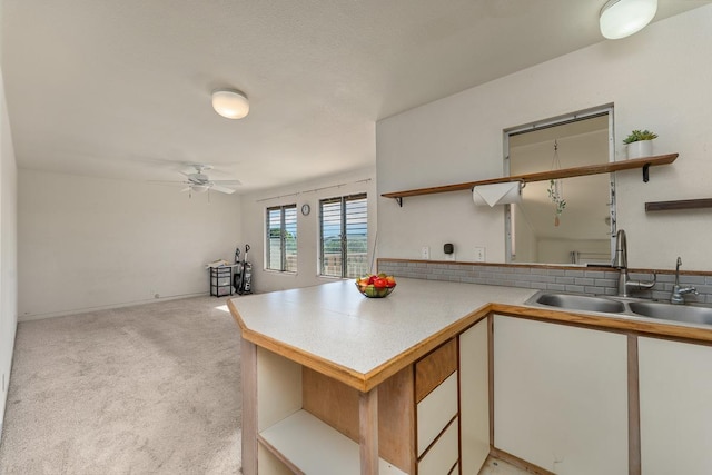 kitchen featuring kitchen peninsula, ceiling fan, sink, light colored carpet, and white cabinetry