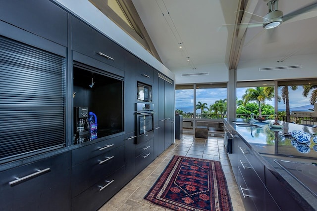 kitchen featuring light tile patterned floors, vaulted ceiling, sink, black microwave, and oven