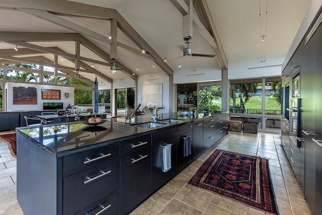 kitchen featuring light tile patterned floors, a center island with sink, ceiling fan, beam ceiling, and a wealth of natural light