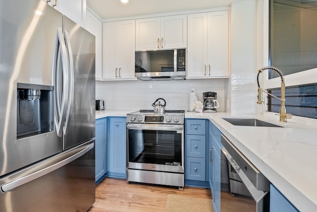 kitchen with sink, appliances with stainless steel finishes, blue cabinetry, white cabinets, and light wood-type flooring