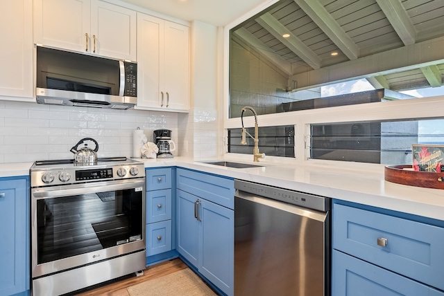 kitchen with stainless steel appliances, sink, blue cabinetry, white cabinets, and lofted ceiling with beams