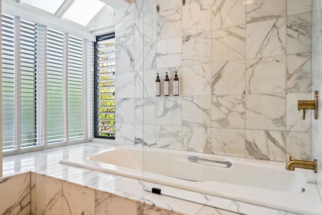 bathroom with a skylight, tile walls, and tiled bath