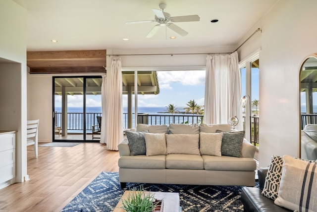 living room featuring light hardwood / wood-style floors, ceiling fan, a water view, and a healthy amount of sunlight