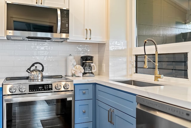 kitchen featuring stainless steel appliances, white cabinetry, sink, blue cabinets, and decorative backsplash